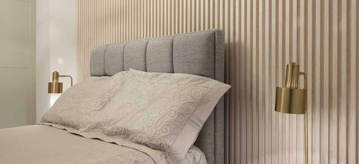 A modern master bedroom featuring walnut slatwall panels behind the bed, showing a floor-to-ceiling installation that adds texture and warmth to an Irish home.