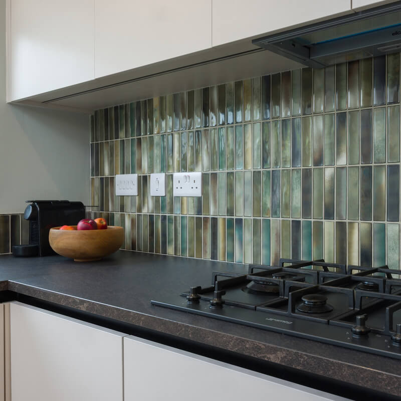 Vertical Green Glazed Backsplash Tiles in Modern Kitchen Vertical green glossy tiles installed as a kitchen backsplash behind a black countertop and gas hob.