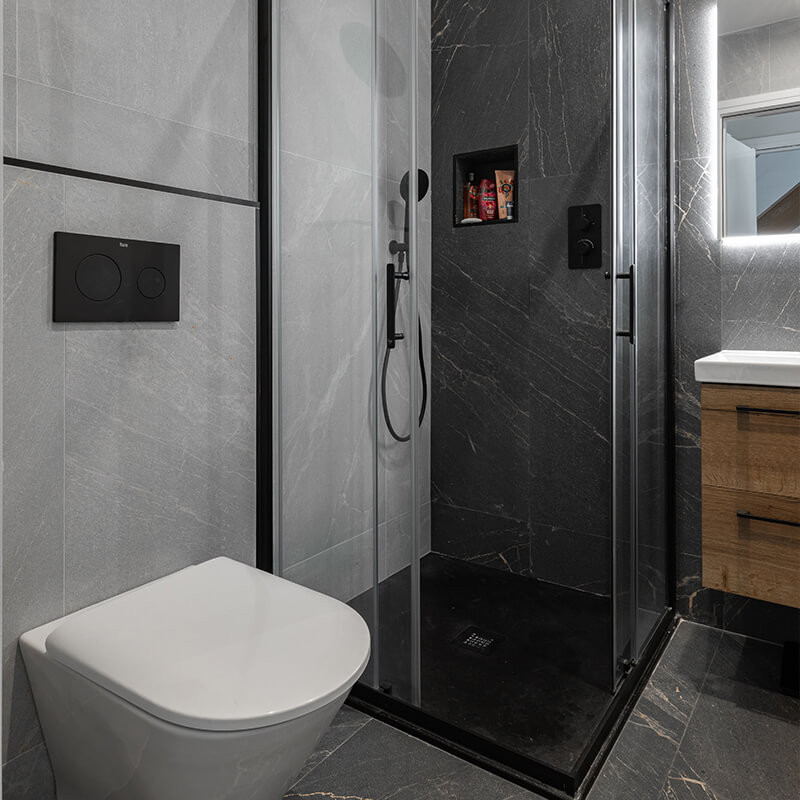 Small bathroom with dark slate-effect shower wall and floor tiles, light grey wall tiles, black-framed glass screen and wall-hung toilet