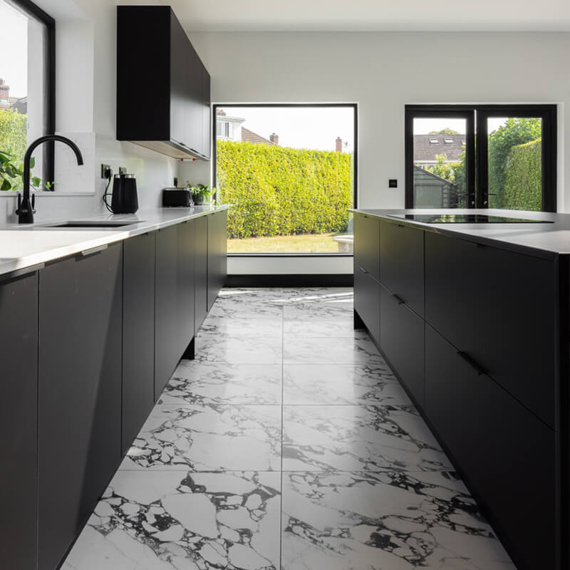 Large-Format Marble-Effect Porcelain Kitchen Floor Tiles Open-plan kitchen with modern black cabinetry and large-format marble-effect porcelain floor tiles leading to a garden door.