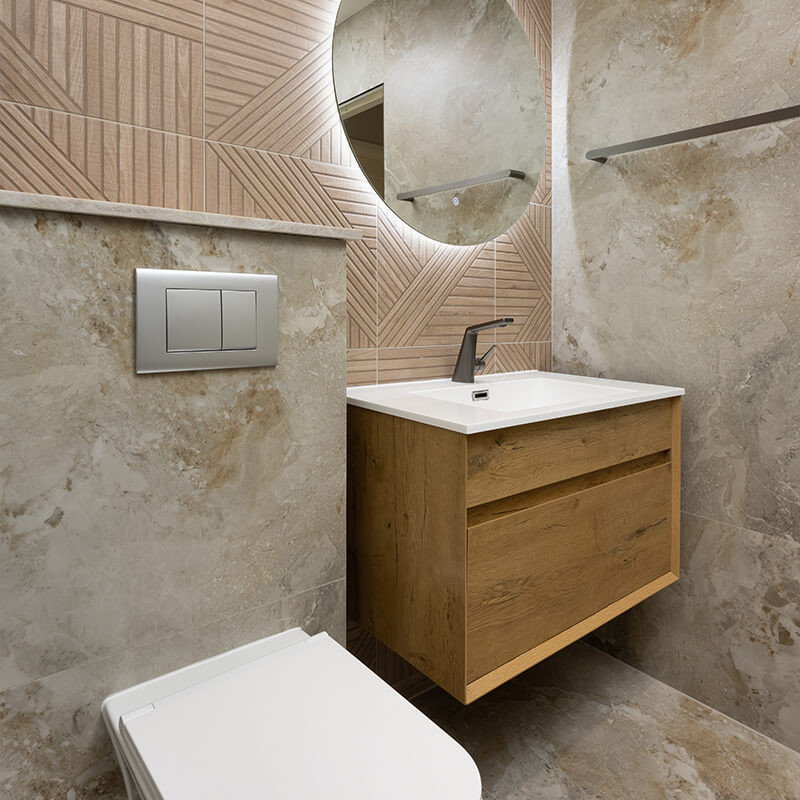 Compact bathroom with large beige stone-effect tiles, pink geometric feature wall tiles, round backlit mirror and floating oak vanity
