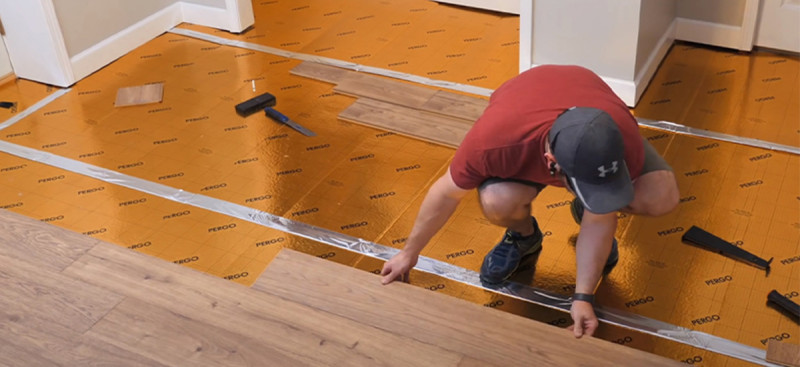 Installing gold foil thermal underlayment for laminate flooring on a concrete subfloor, showing the vapor barrier seal and cushioned insulation for an Irish home.