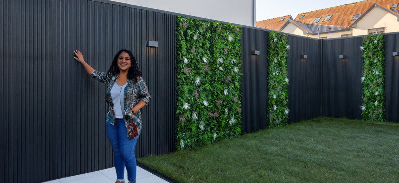 A woman standing in a modern back garden next to a wall featuring stylish dark wood exterior cladding panels.